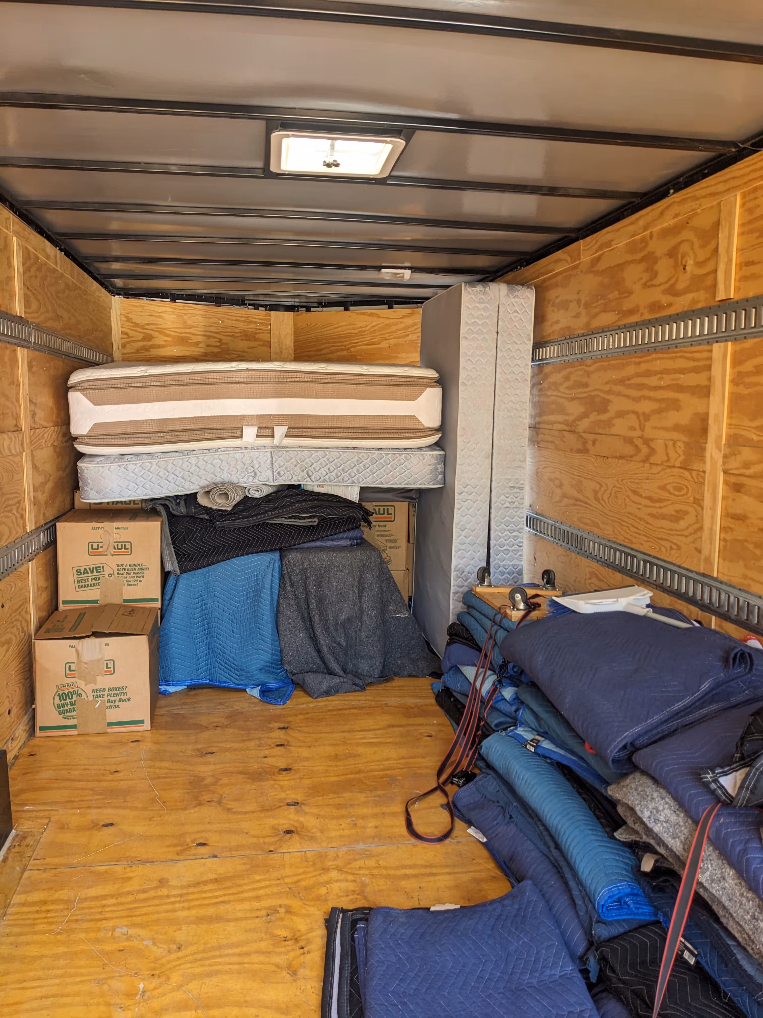 Interior of a moving truck loaded with stacked mattresses, packed boxes, and folded moving blankets.