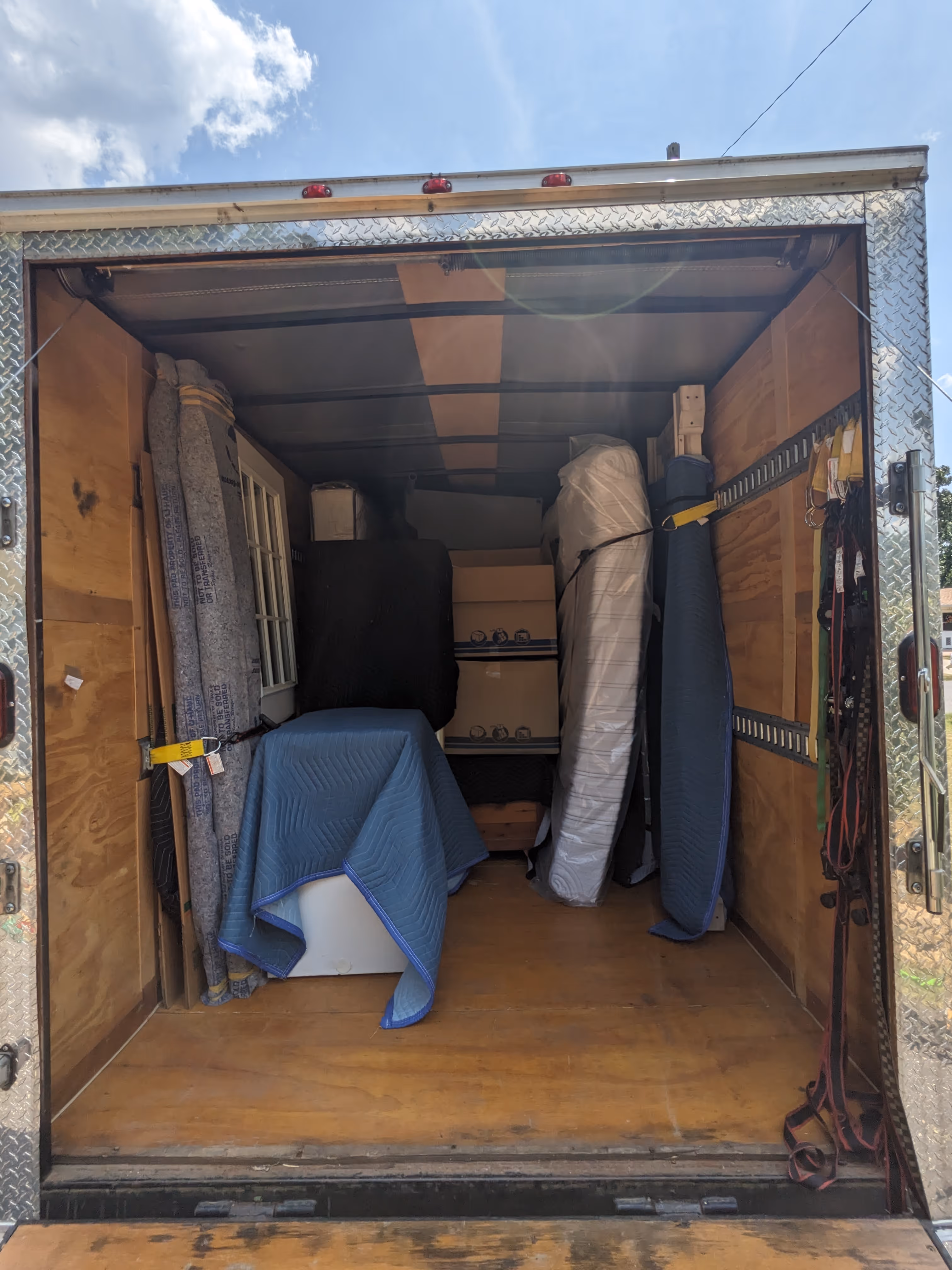 Open moving truck loaded with wrapped furniture, boxes, a door, and various moving blankets secured inside.