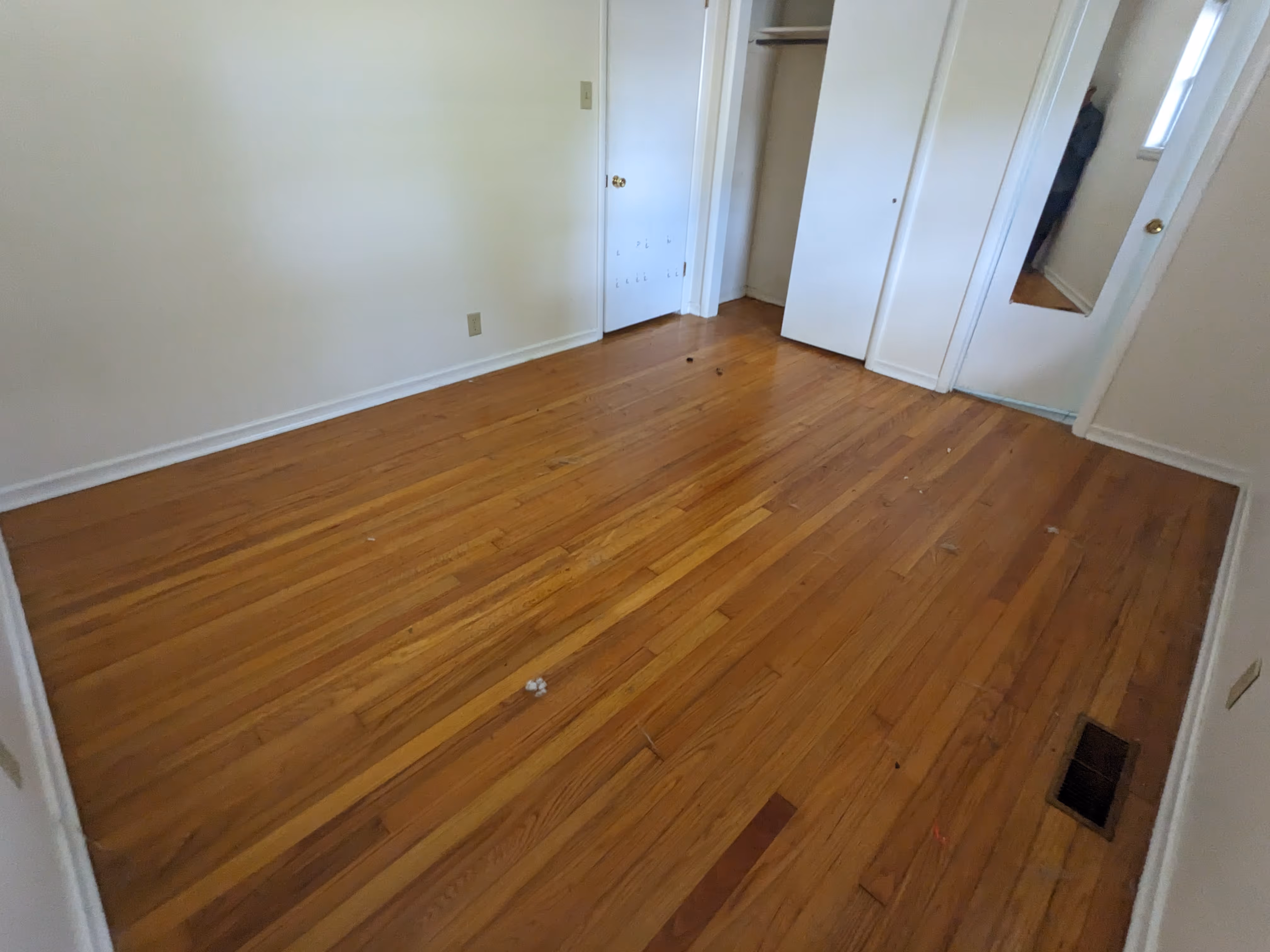 Empty room with wooden floor, white walls, a door with a full-length mirror, and a closet with sliding doors.