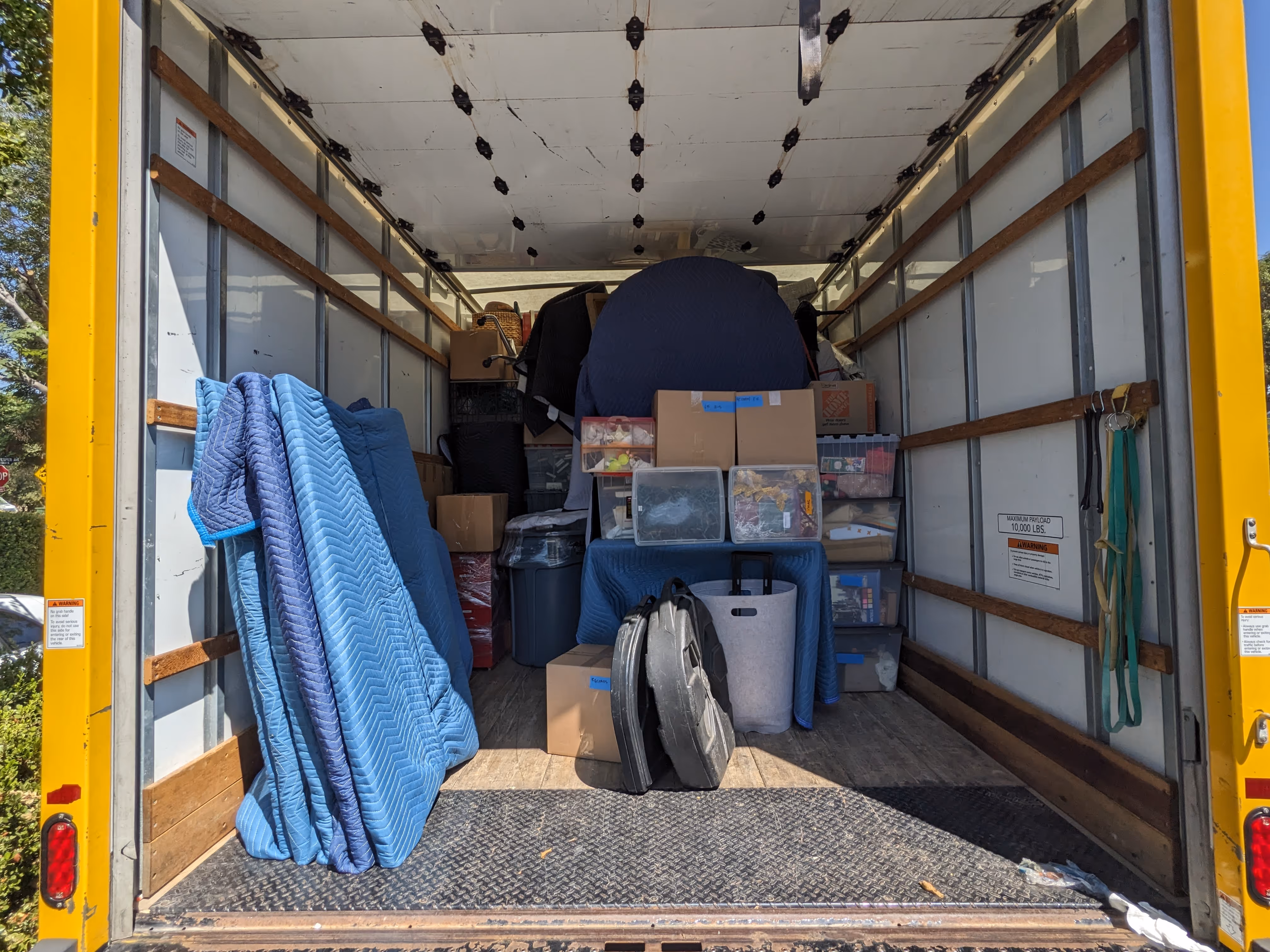 Open yellow moving truck filled with stacked moving blankets, cardboard boxes, and plastic storage bins.