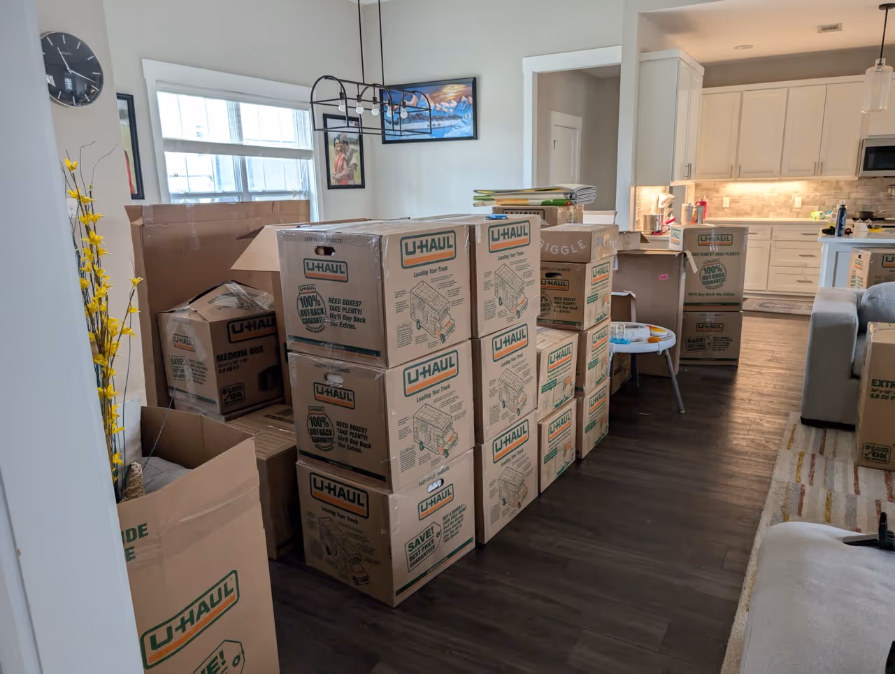 Living room and kitchen area filled with stacked U-Haul moving boxes and packed furniture.