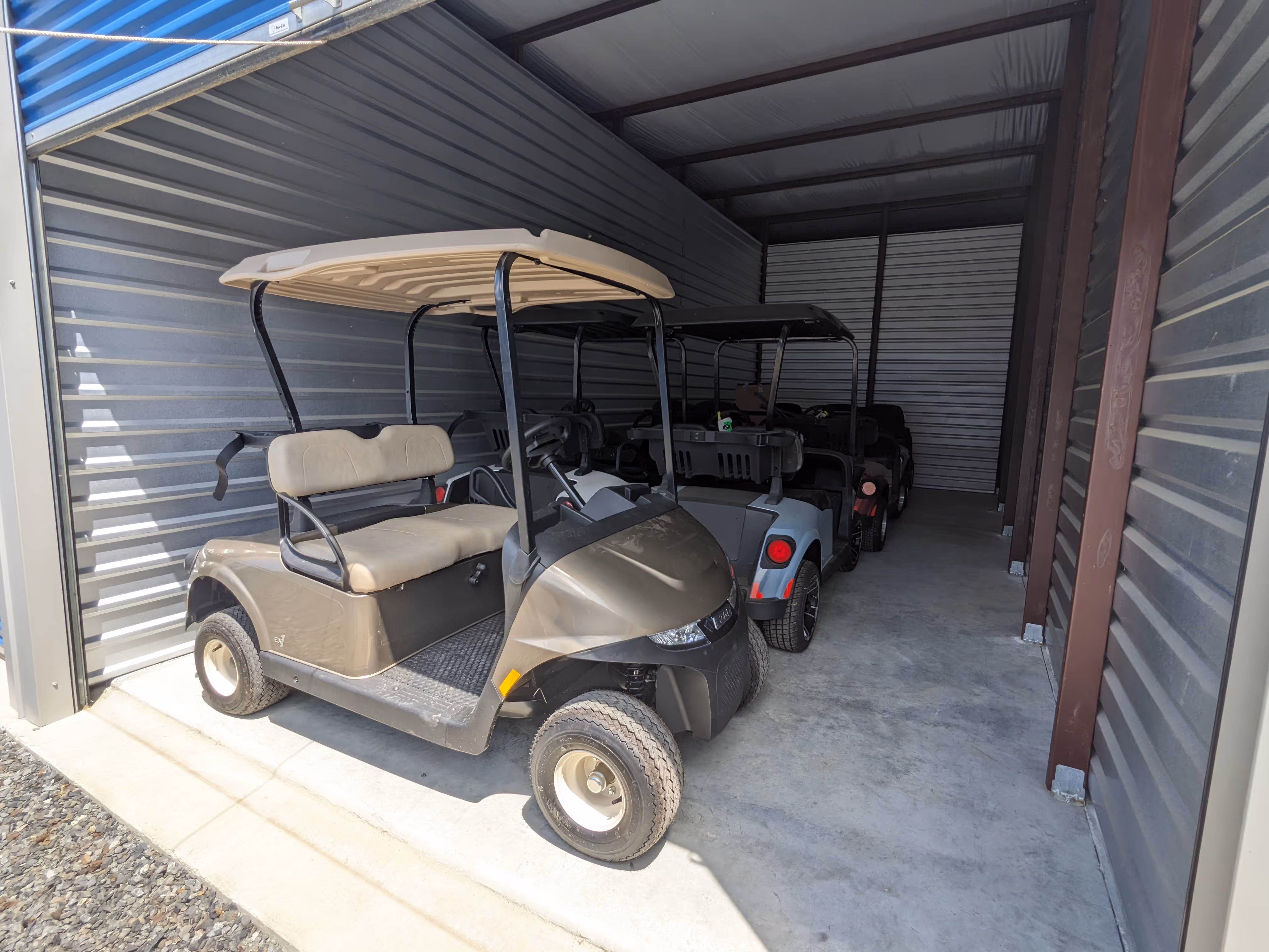 Brown golf cart parked inside a metal storage unit with other golf carts behind it.