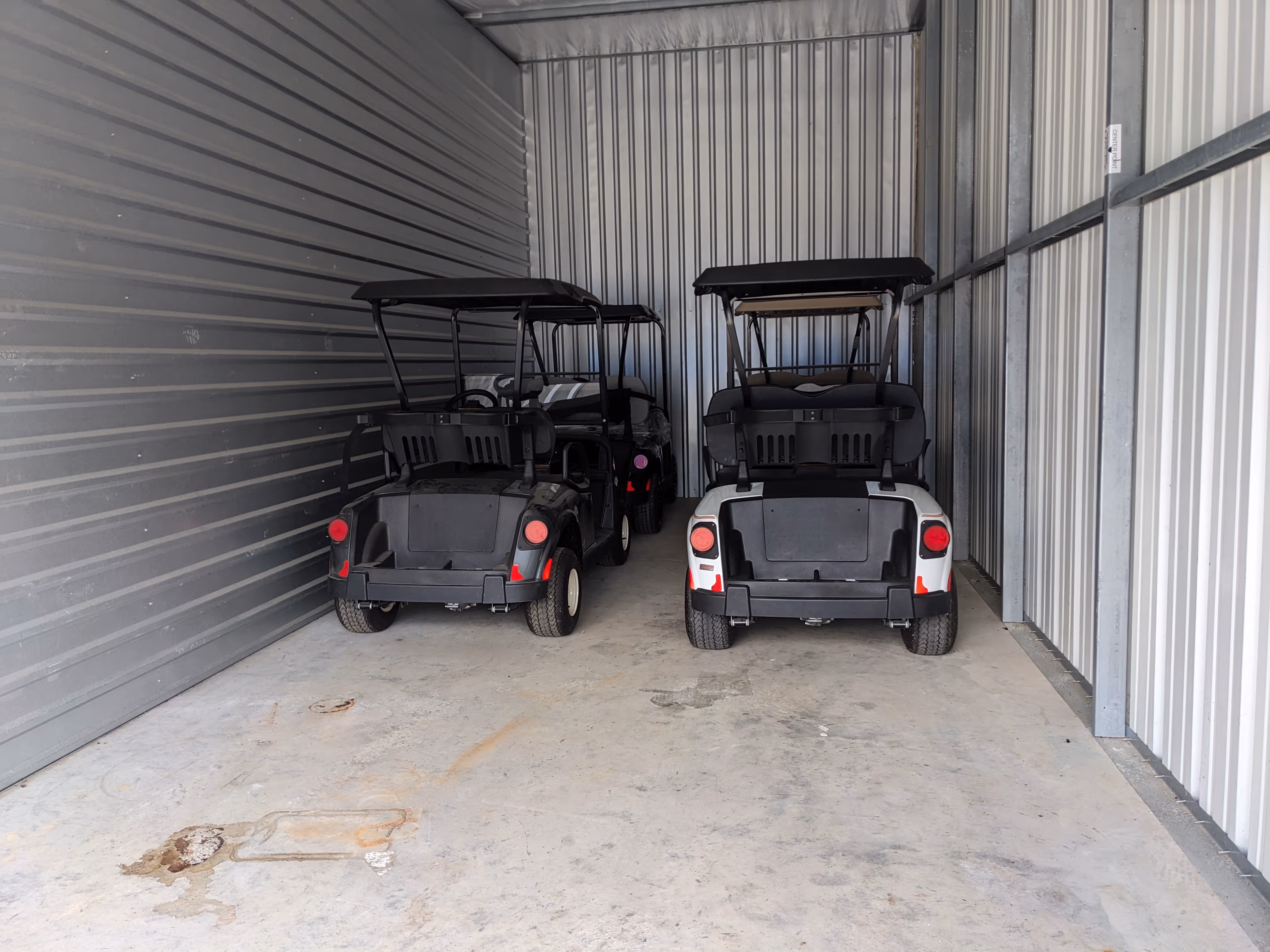 Three golf carts parked inside a metal storage unit with concrete floor and corrugated metal walls.