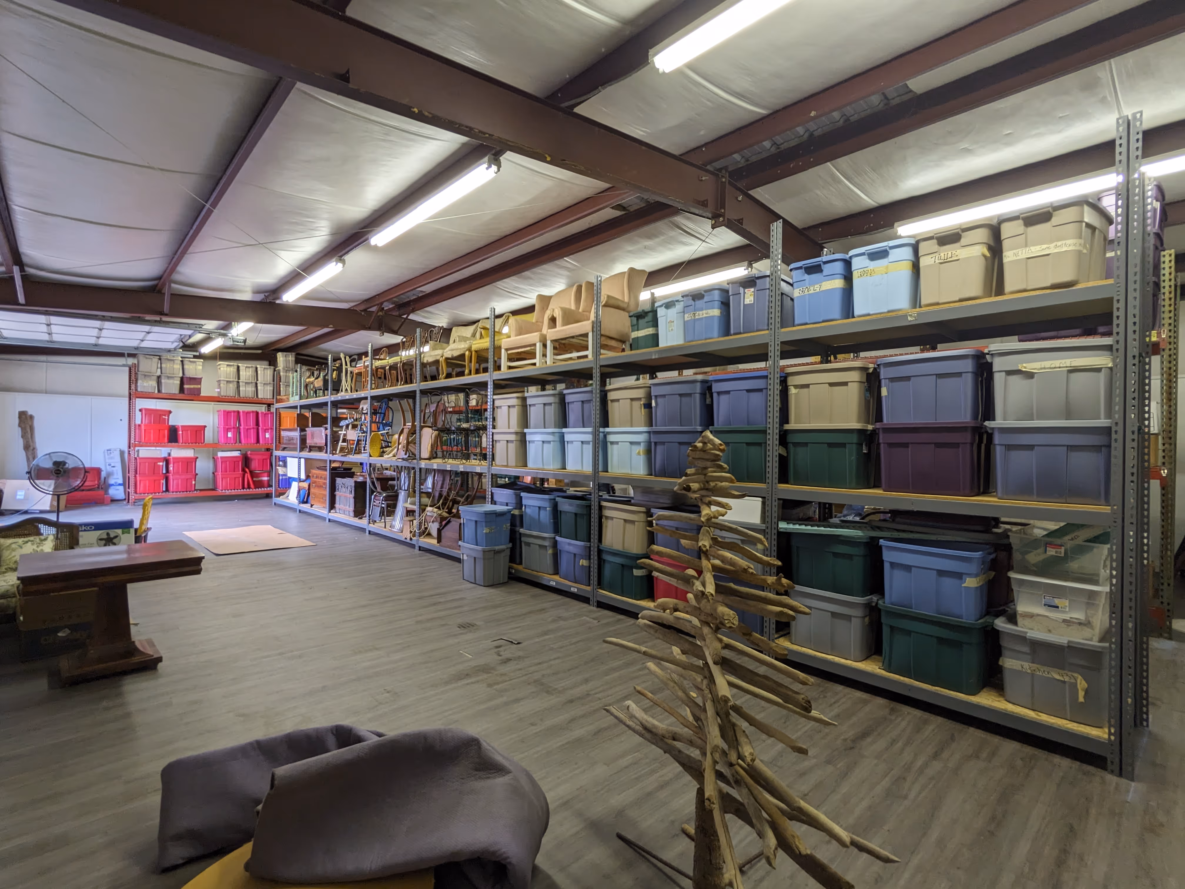 Storage room with shelves filled with labeled plastic bins and a wooden structure resembling a tree in the center.