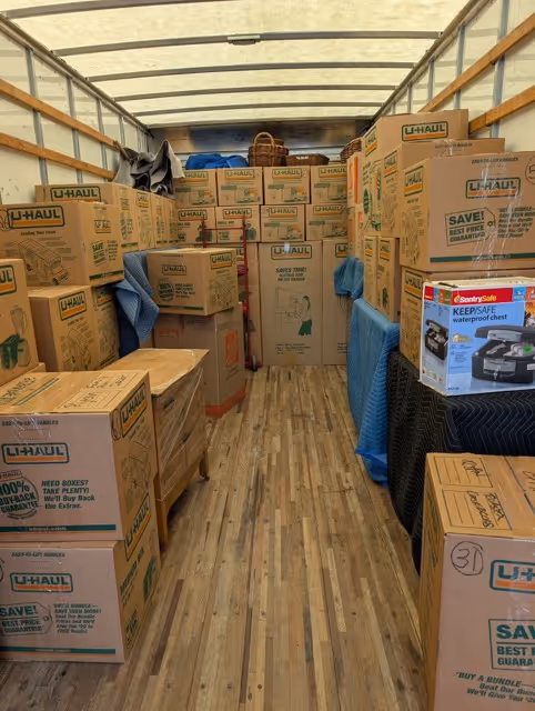 Interior of a moving truck packed with stacked U-Haul boxes and a SentrySafe waterproof chest box on the right side.