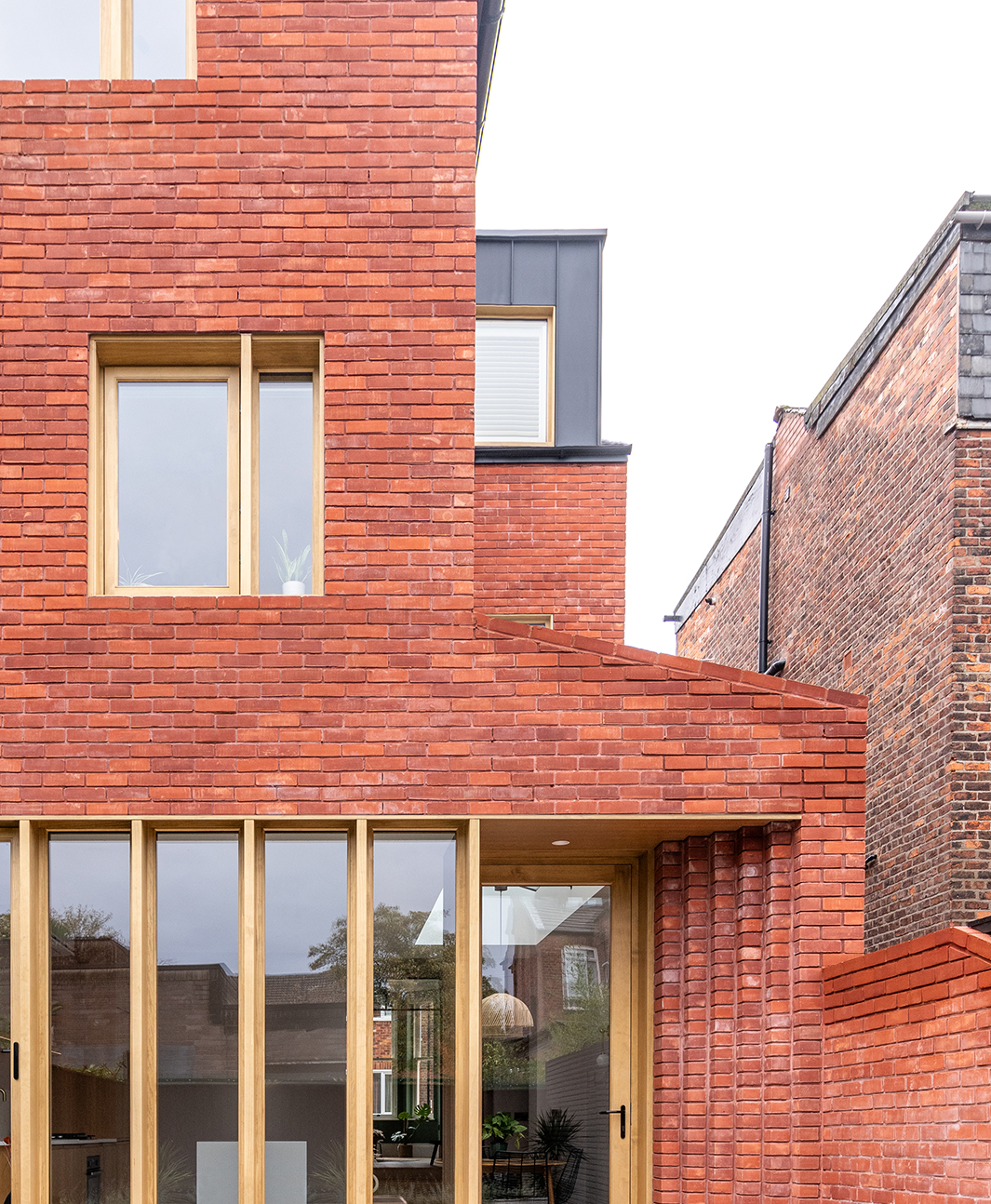 A red brick Victorian terraced house with stepped brickwork and a contemporary timber framed glazed screen in Chorlton, Manchester.