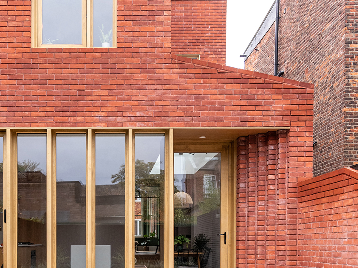 A red brick Victorian terraced house with stepped brickwork and a contemporary timber framed glazed screen in Chorlton, Manchester.