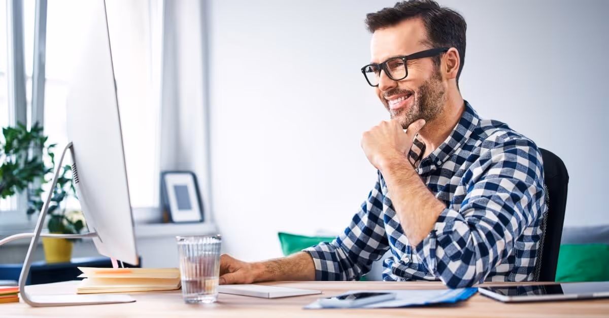 A man wearing glasses and a plaid shirt is sitting at a desk.