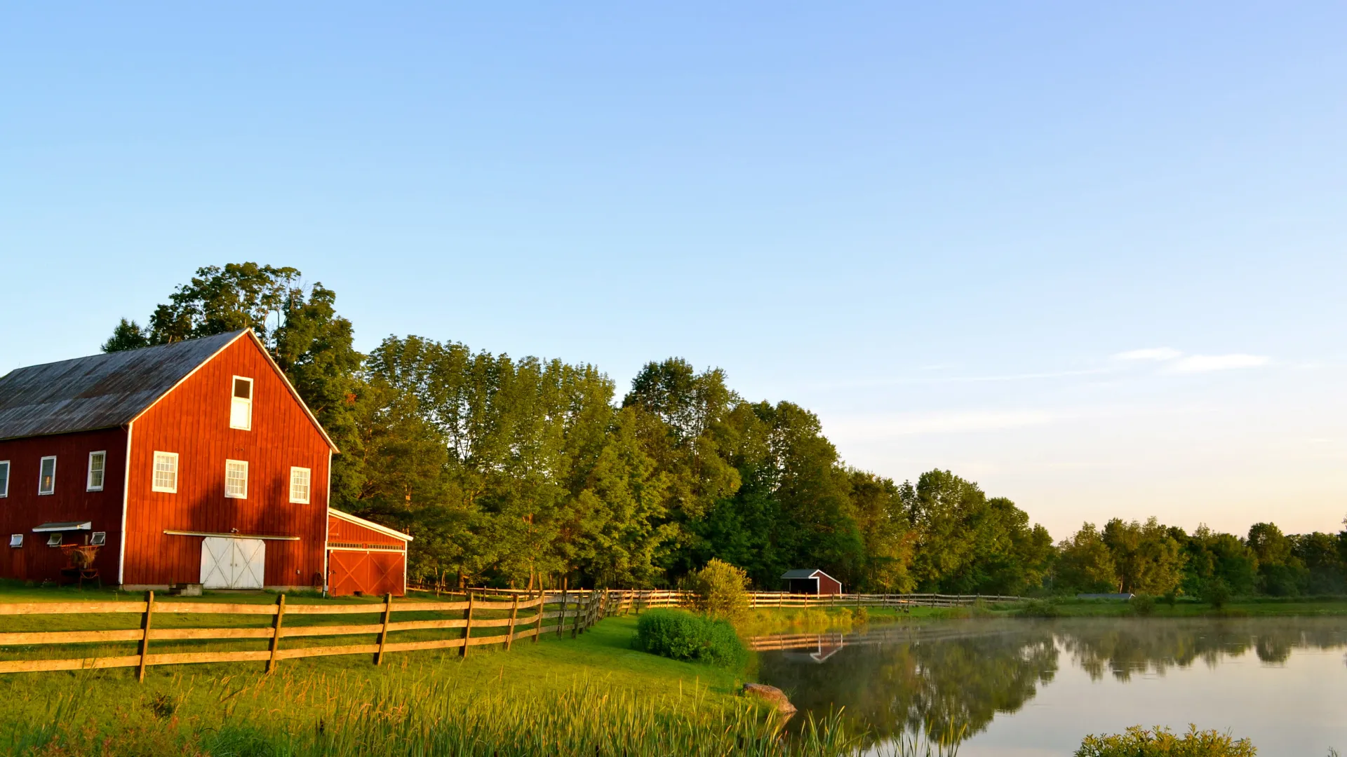 Röd ladugård och bondgård i vackert landskap vid vattnet. solceller för lantbruk.