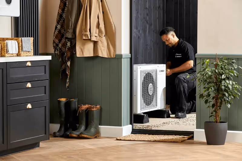 An engineer fixing a worcester bosch on the porch of a house with the photo taken from inside the house