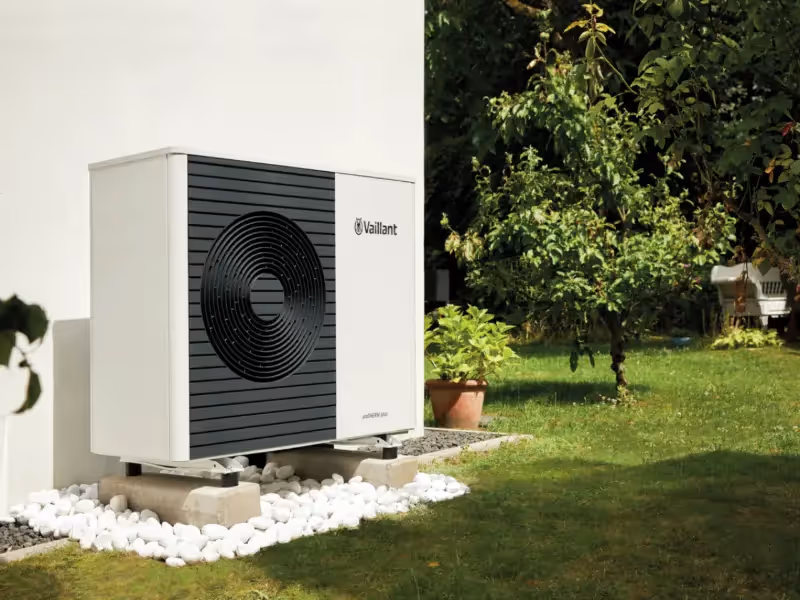 AN image of a Vaillant AroTherm Plus in the garden on a concrete base among white stone and against a white house