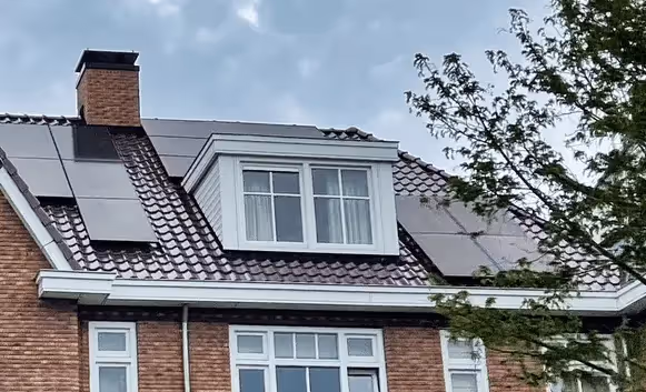 A picture of a house with solar panels on the roof around a dormer and chimney