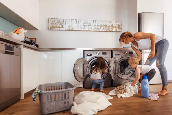 A woman and two children pulling washing out of a washing machine and a tumble dryer