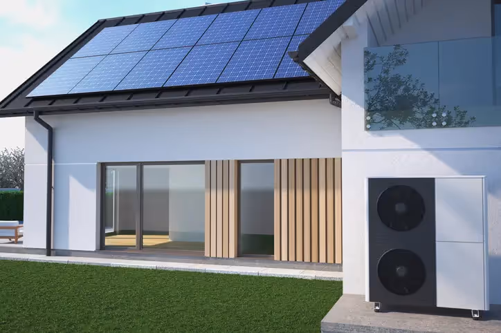A modern looking home with solar panels on the roof and a heat pump by the side of the house