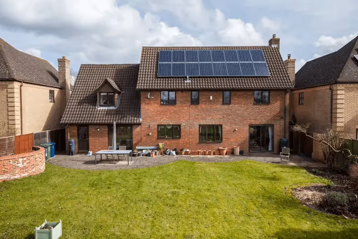 A picture of a house from the end of a lawned garden showing solar panels on the roof