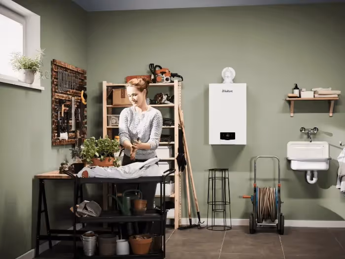 A woman plating a potted plant with a Vaillant boiler on the wall behind her