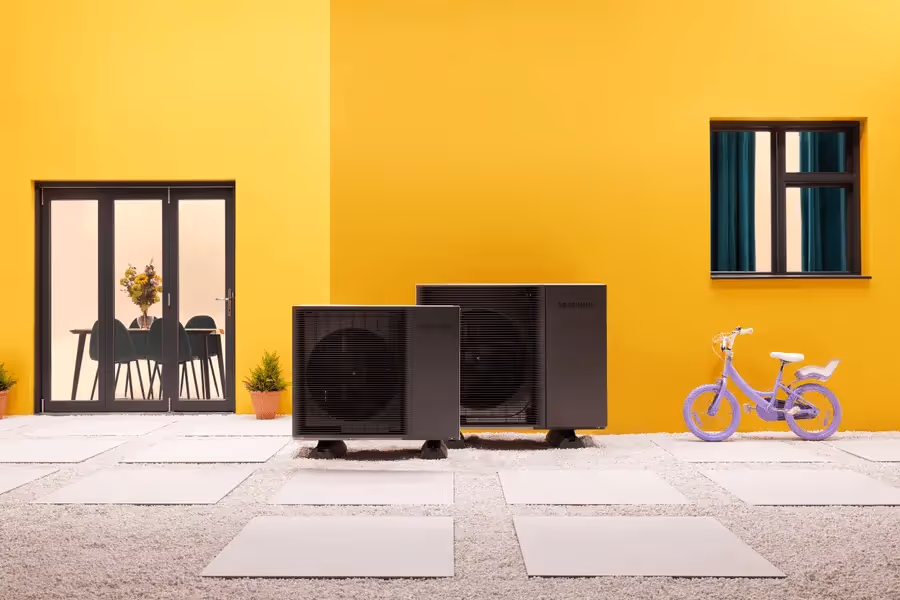 Two Samsung EHS black monoblock heat pumps outside a house with yellow walls