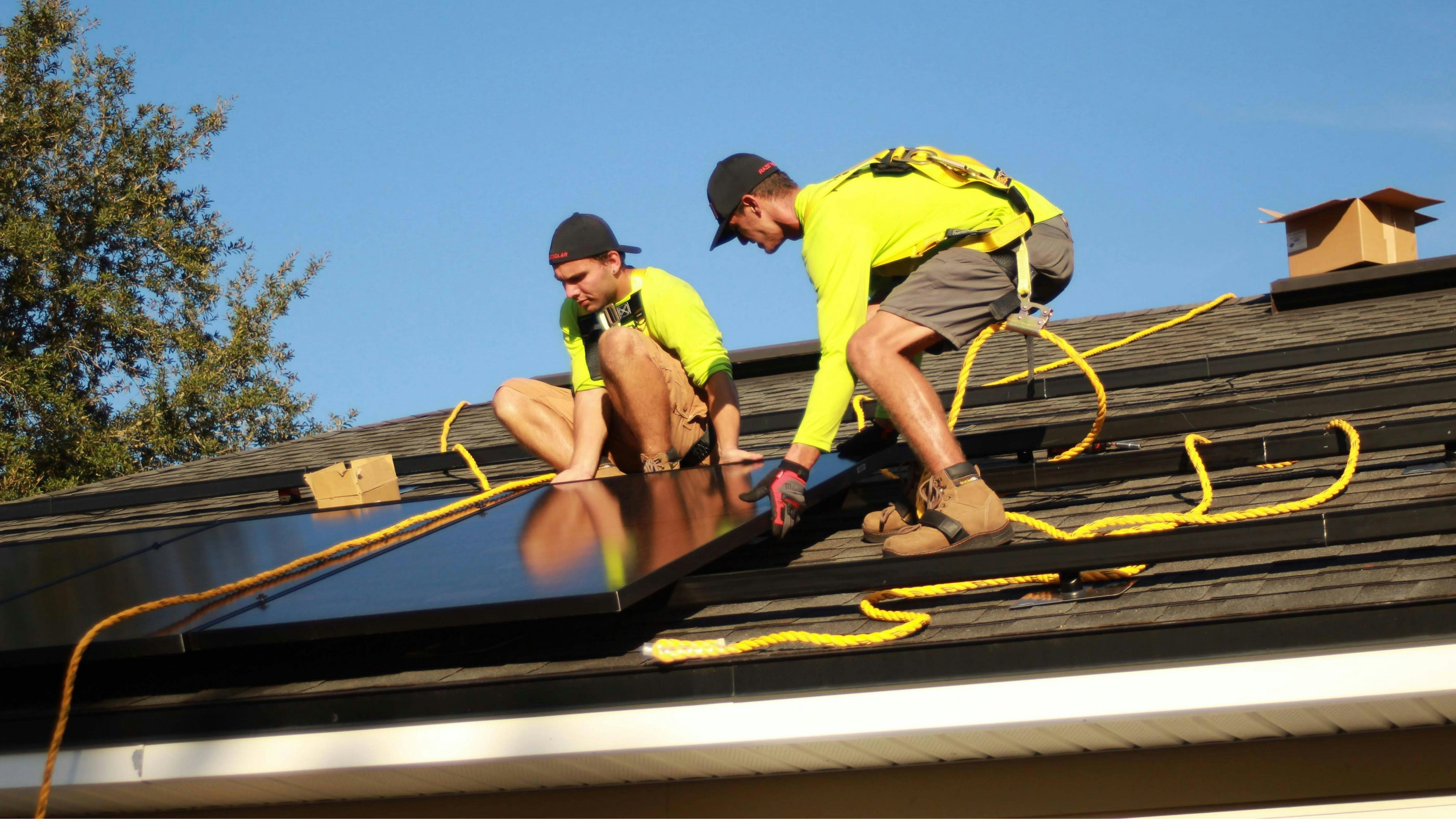Solar installers on a roof using harnesses to fit all black solar PV panels