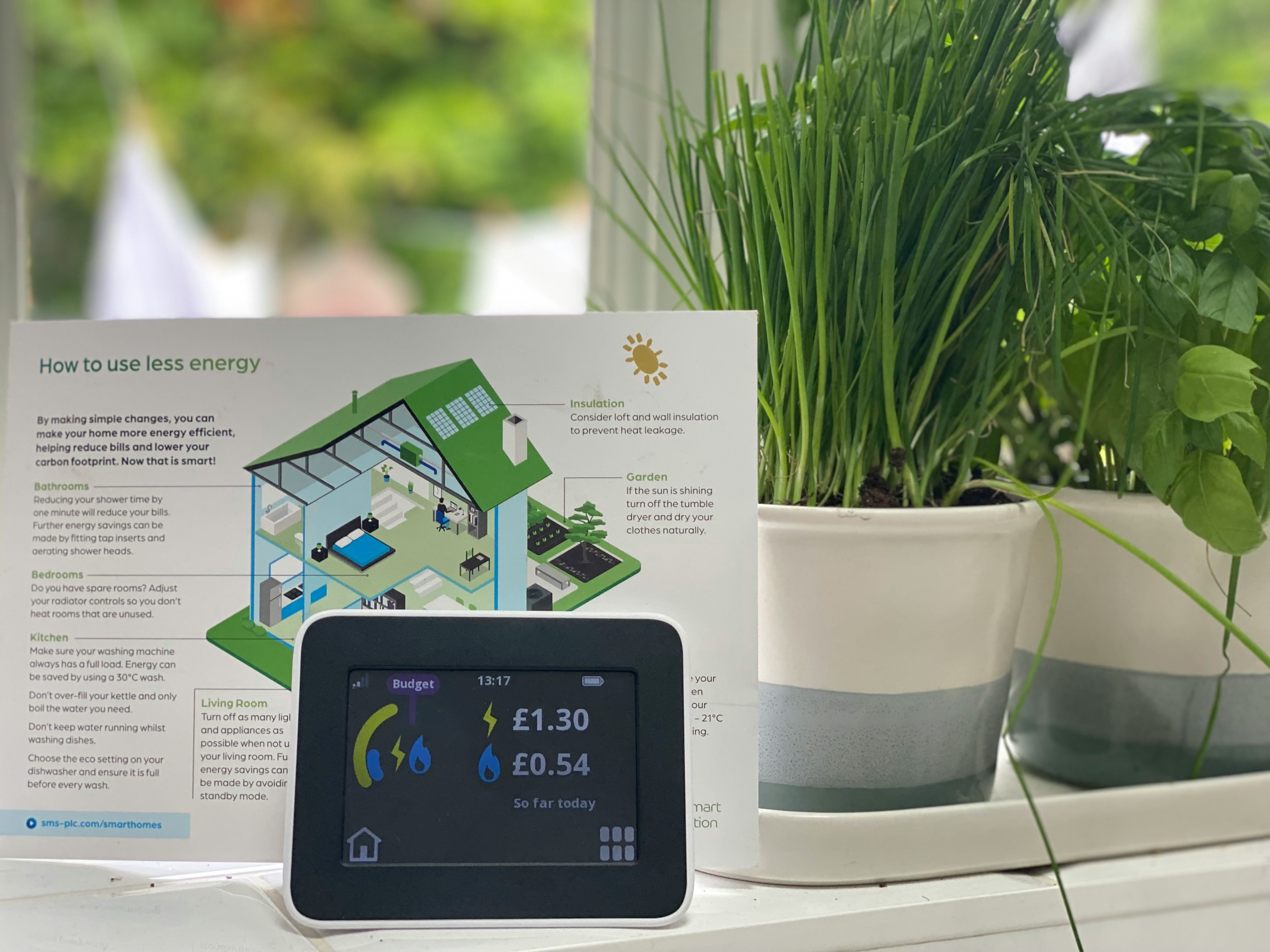An image f a smart meter monitor showing household energy use and a leaflet behind it explaining how to use less energy