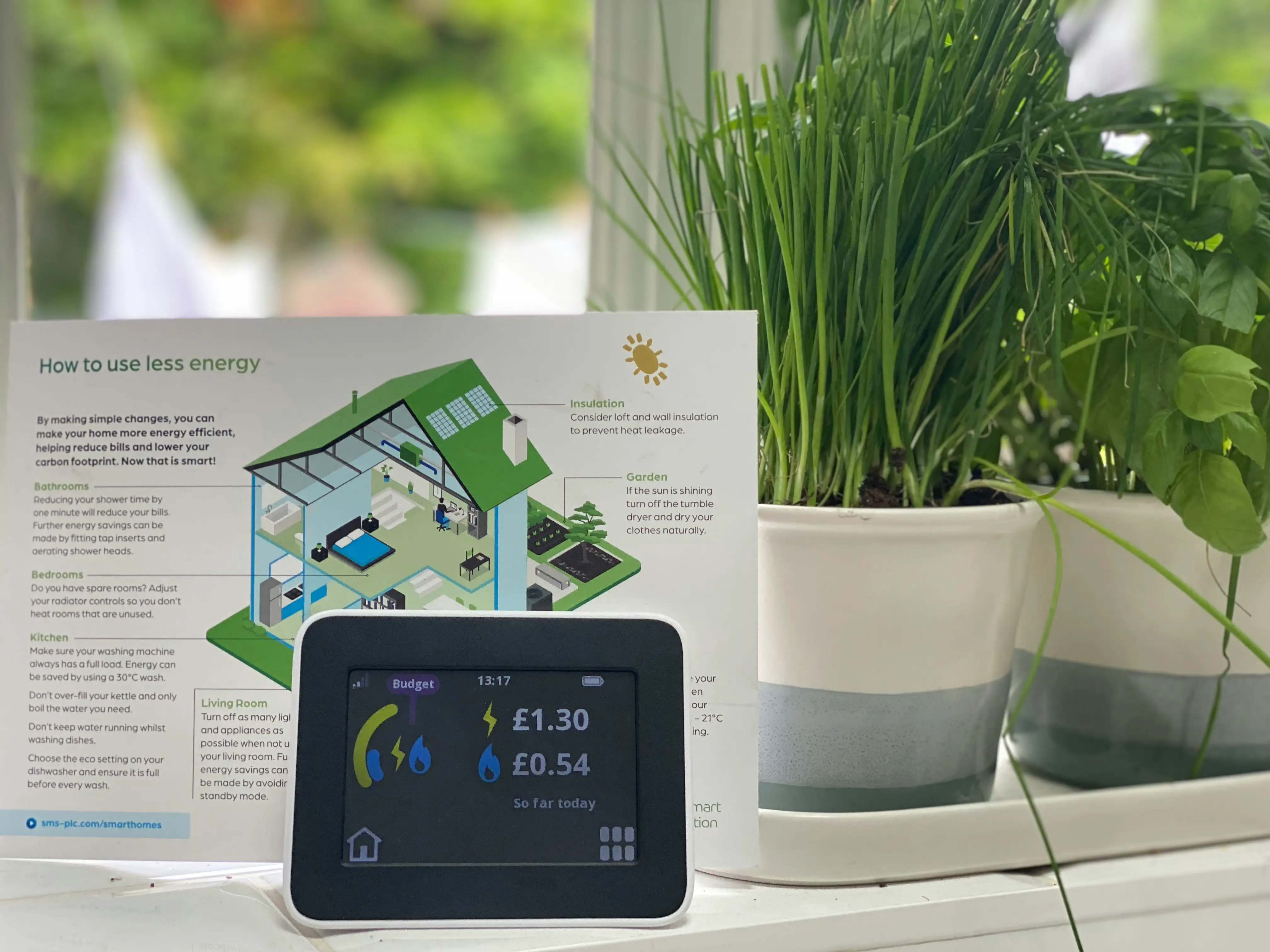 An image f a smart meter monitor showing household energy use and a leaflet behind it explaining how to use less energy