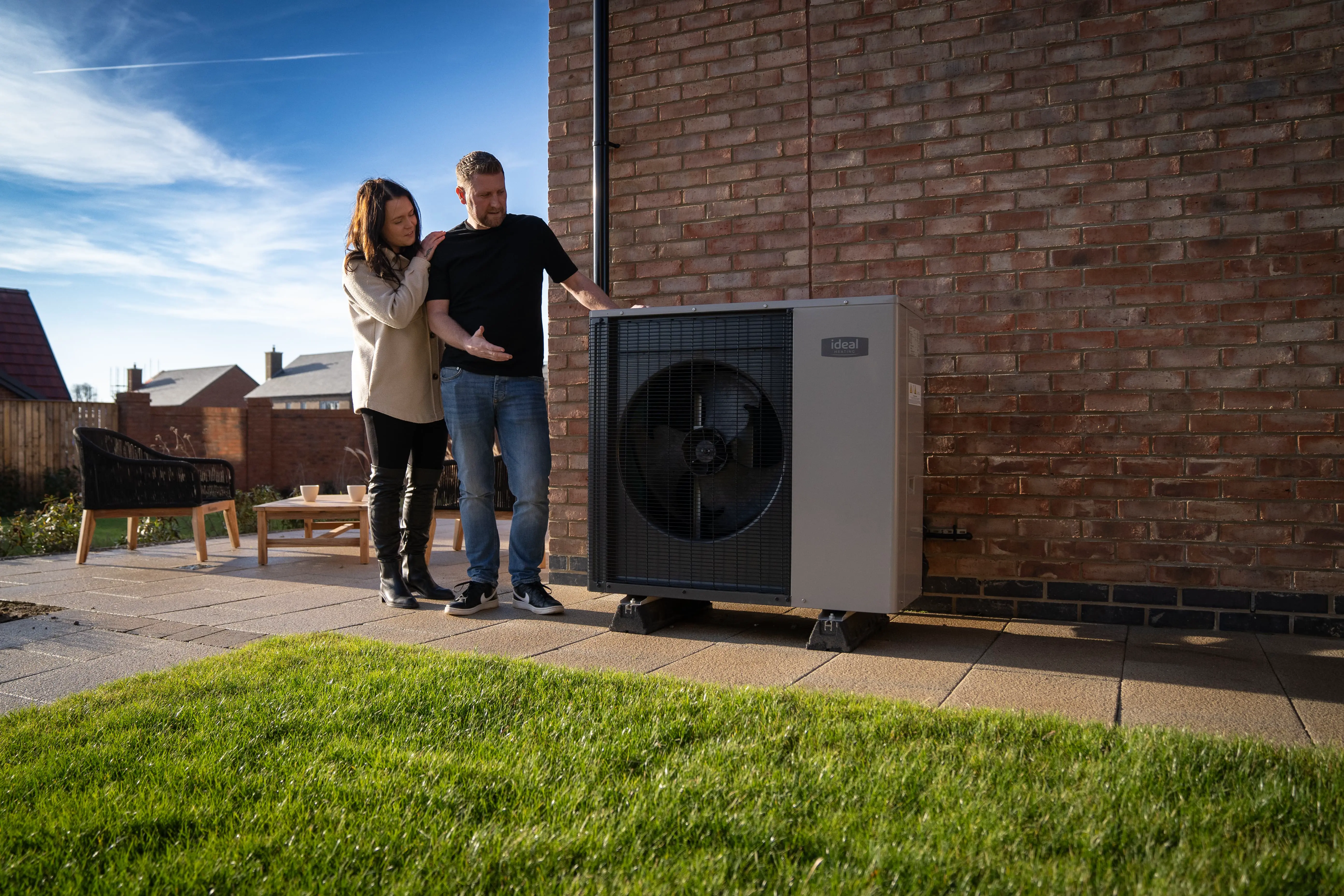Image of an ideal logic air heat pump outside a house, by a bench in the sun