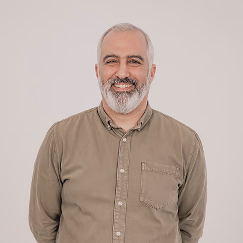 Smiling middle-aged man with gray hair and beard wearing a brown button-up shirt.