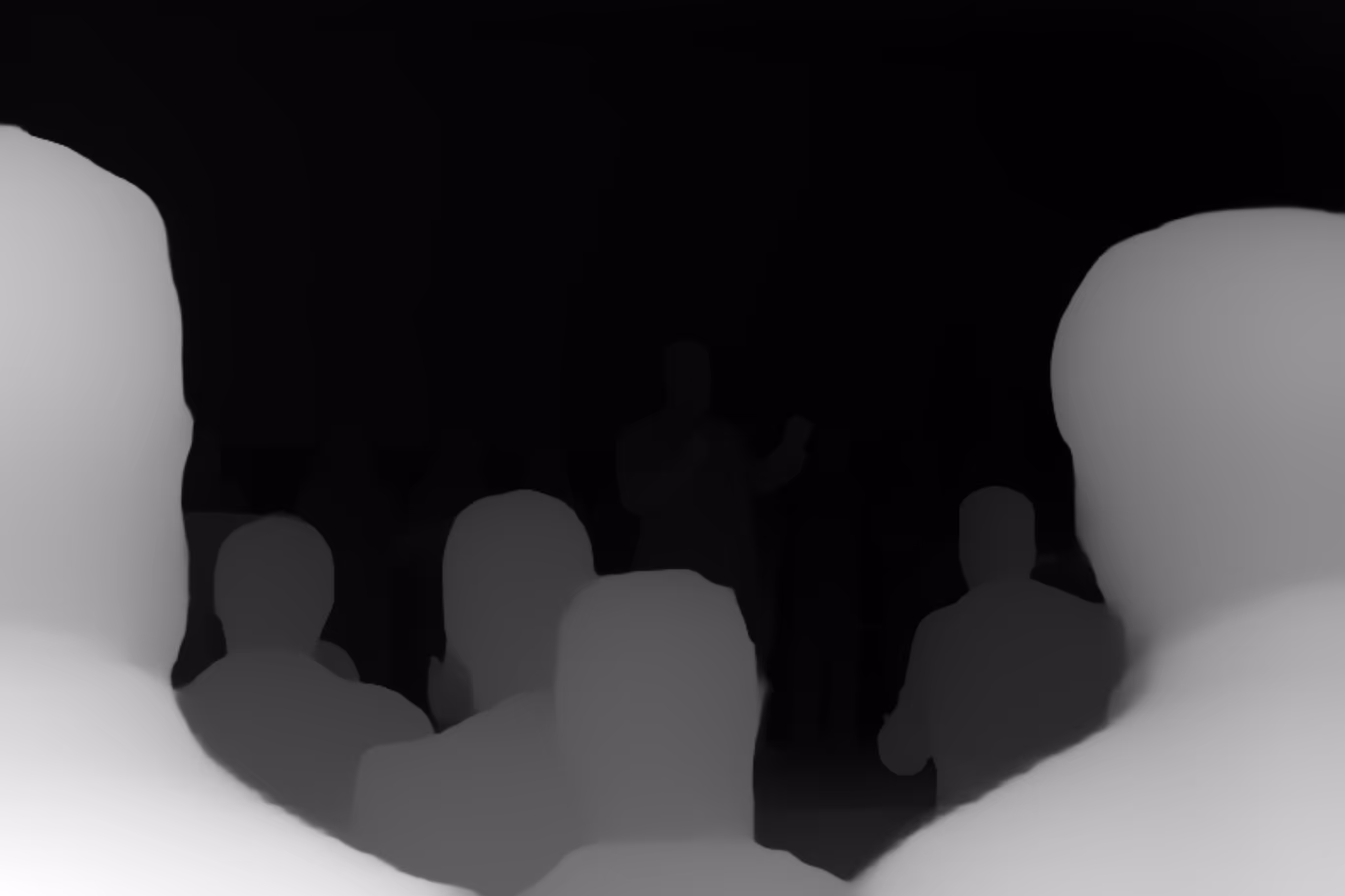 Silhouettes of an audience watching a person speaking on stage against a dark background.