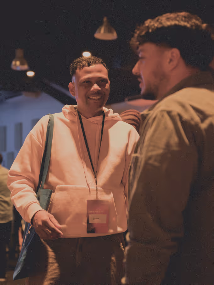Two men engaged in a conversation at an indoor event with dim lighting.