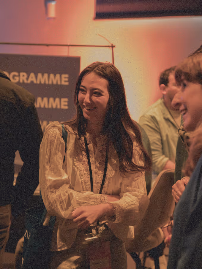 Smiling woman in a cream lace blouse with a lanyard, interacting at an indoor event.