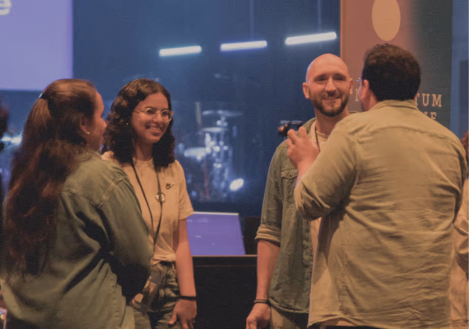 Four people engaged in conversation at an indoor event with stage lights and musical instruments in the background.