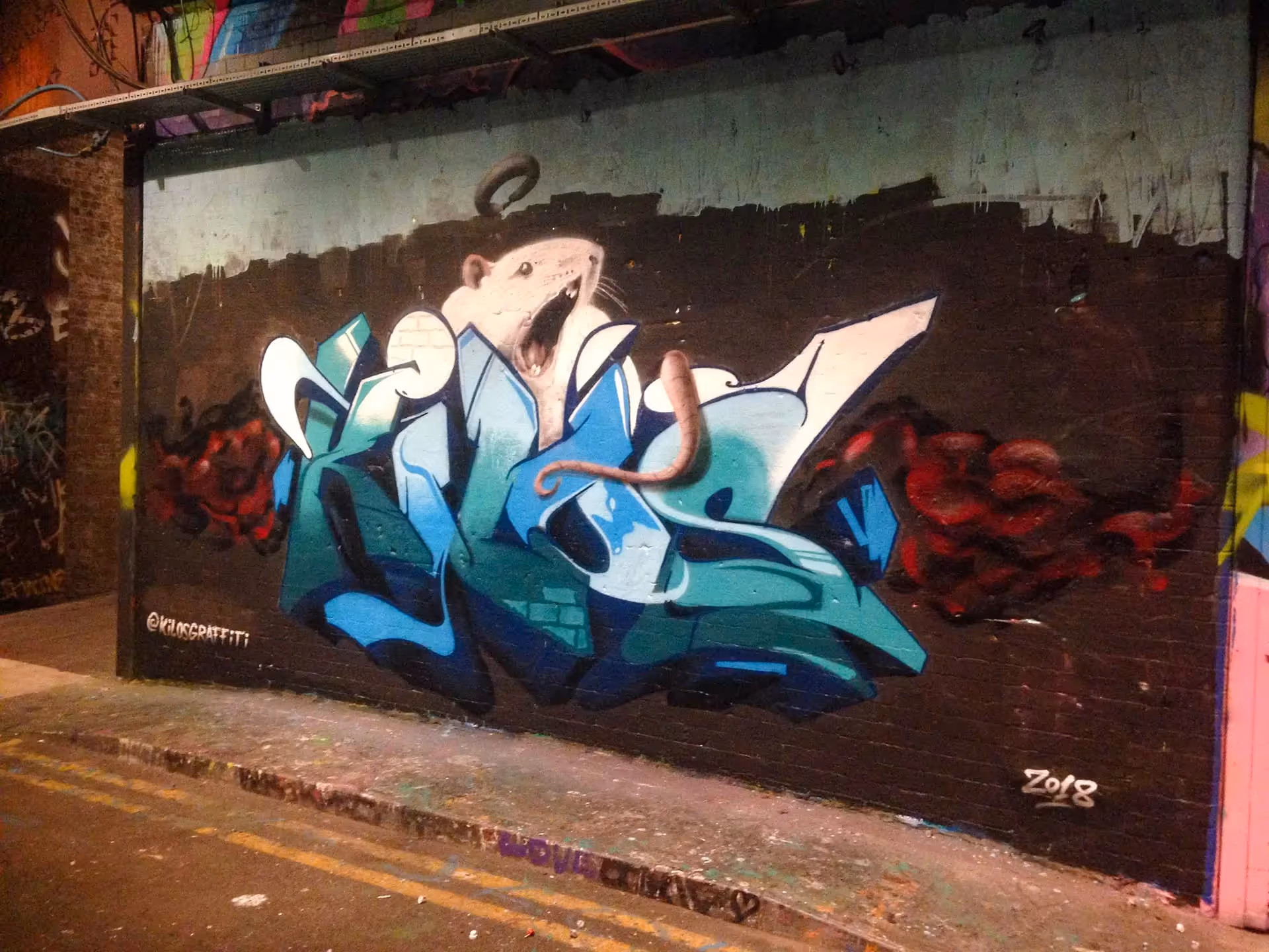 A blueish Kilos graffiti piece with a realistic rat painted on top of it