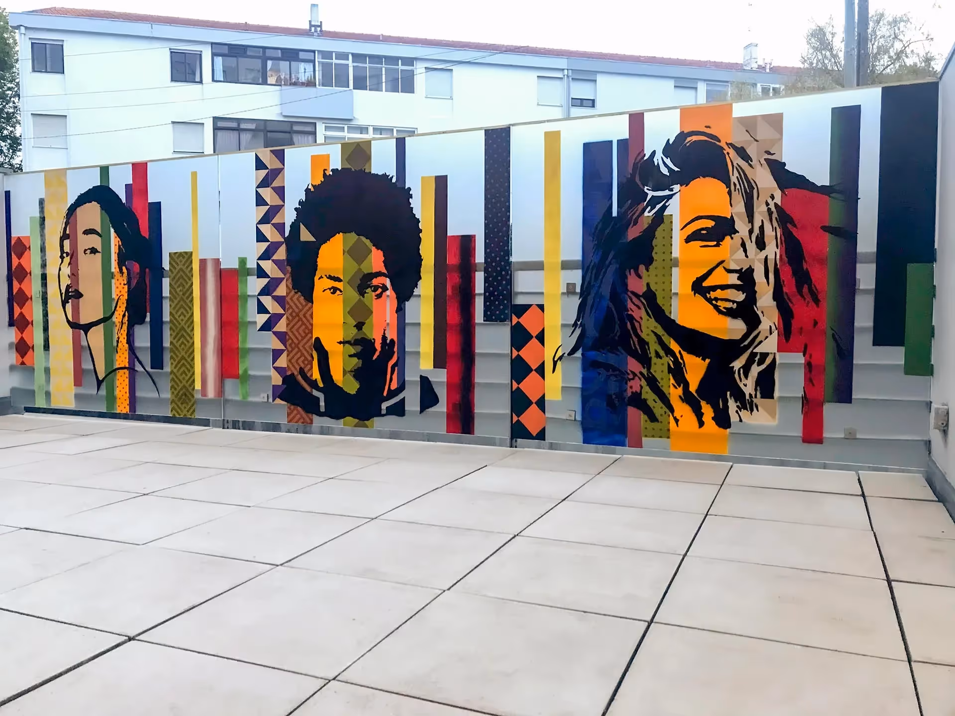 Stencil painting of three young adult faces from different continents on a colored background of vertical stripes