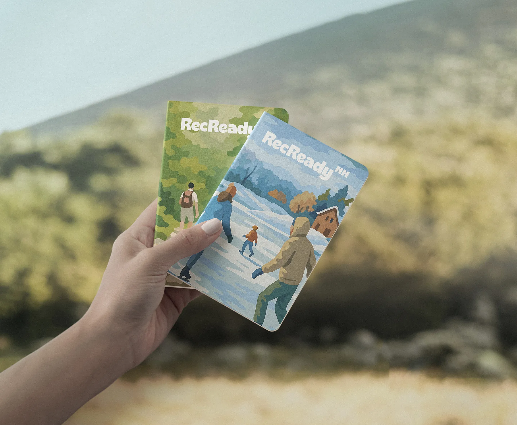 Hand holding two notebooks with illustrations on the covers.
