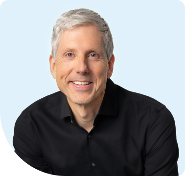 Smiling middle-aged man with gray hair wearing a black button-up shirt against a pale blue background.