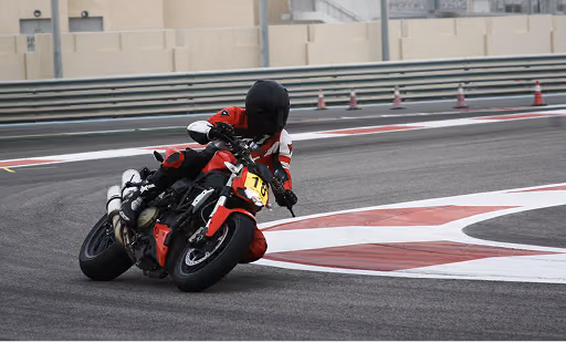 Motorcyclist in red and black gear leaning into a sharp curve on a race track.