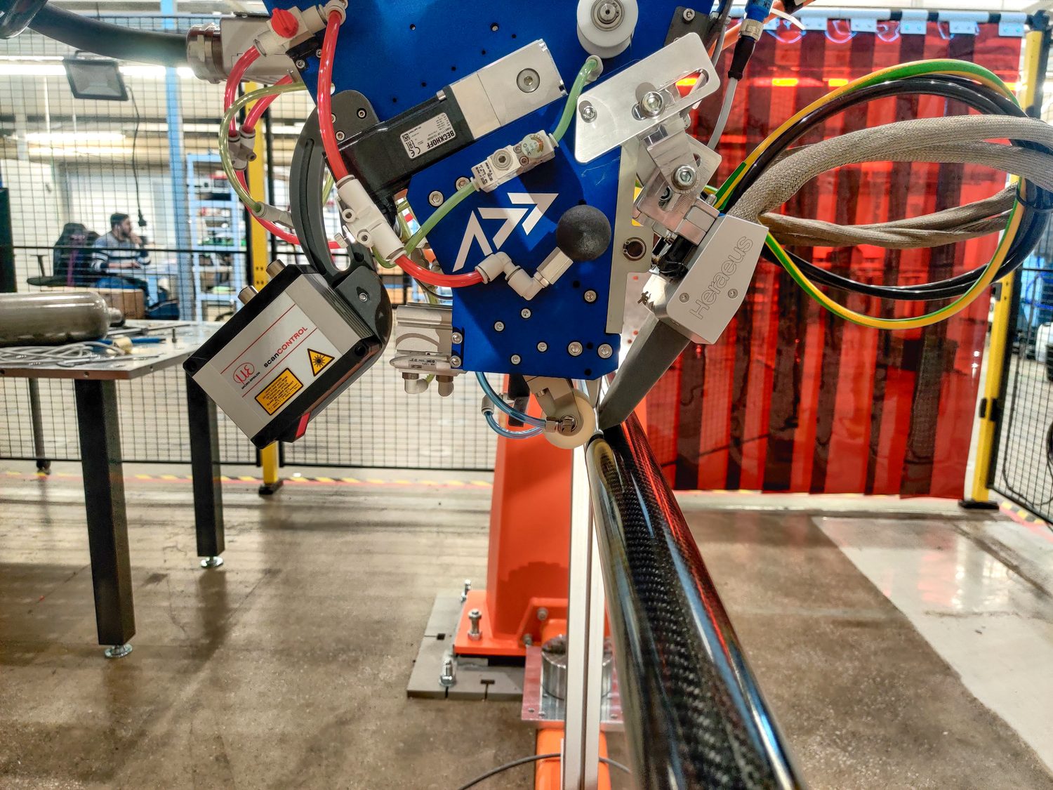 The Addcomposites AFP-XS head placing carbon fiber onto a tubular part, with an integrated laser profilometer and heat module.