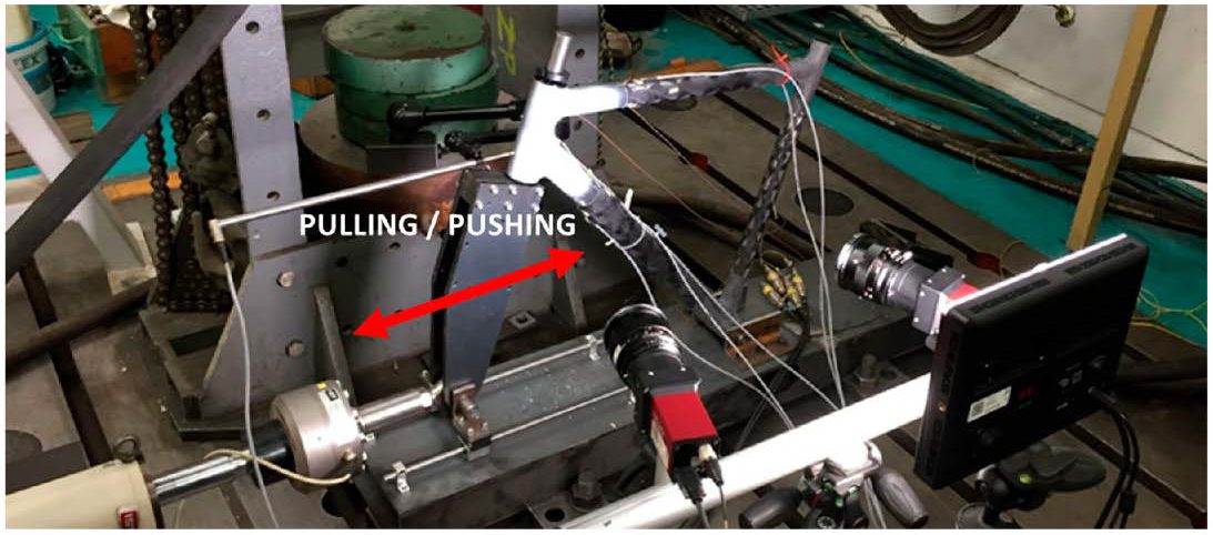 Structural strength test setup: a simplified front-triangle specimen mounted in the test bed and loaded horizontally by a servo-hydraulic actuator.