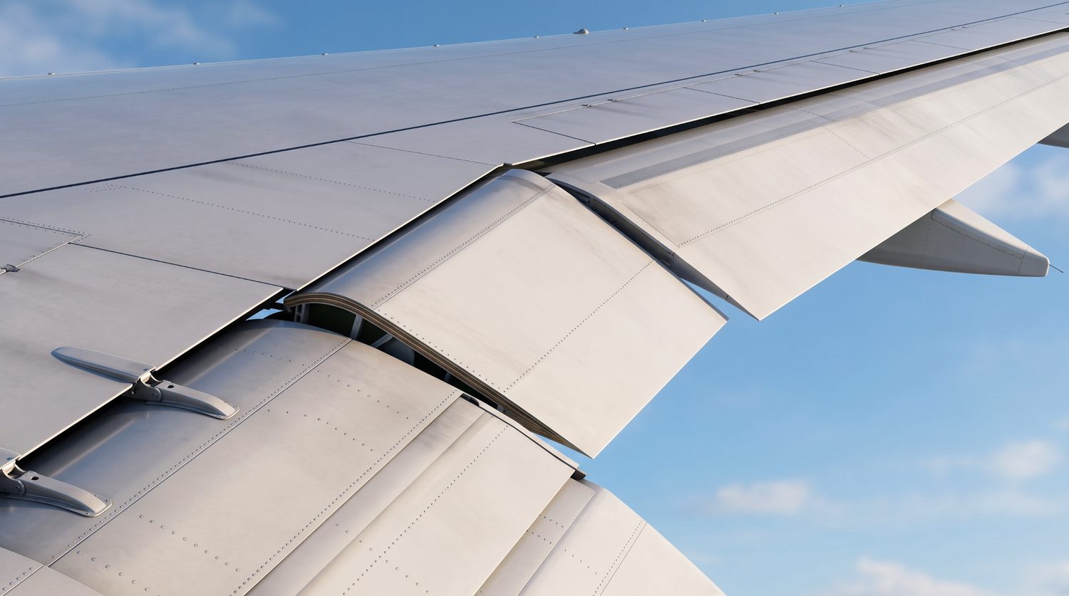 A flap-aileron control surface (flaperon) shown in the deflected position on the wing trailing edge, illustrating the hinged, load-bearing architecture that makes such flight-critical components challenging to manufacture at production rate.