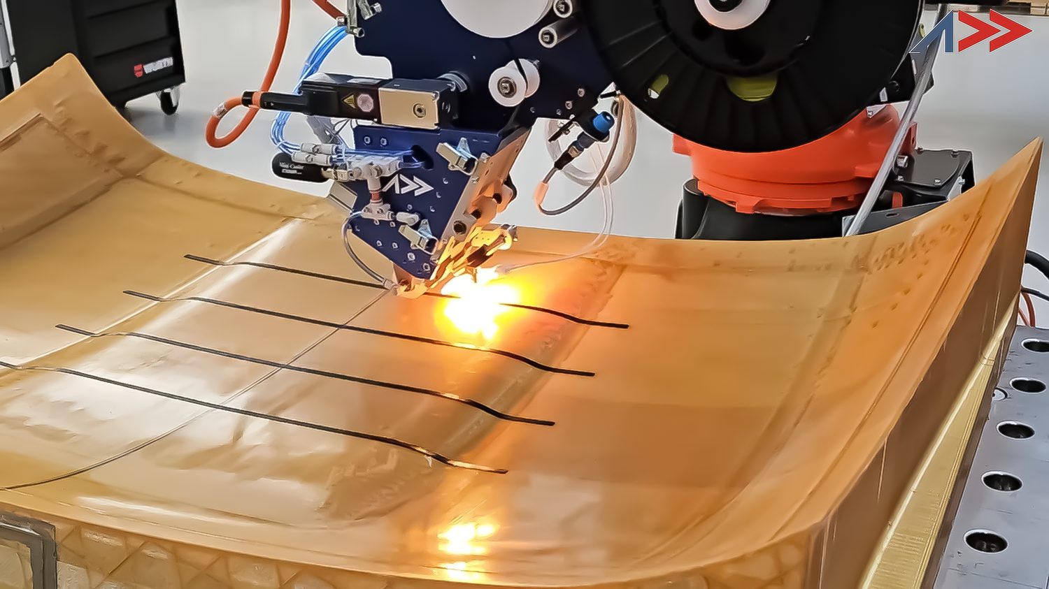 Close-up of the Addcomposites AFP-XS head laser-heating and depositing carbon tow onto a double-curvature thermoplastic mould, ADD logo visible on the toolhead.