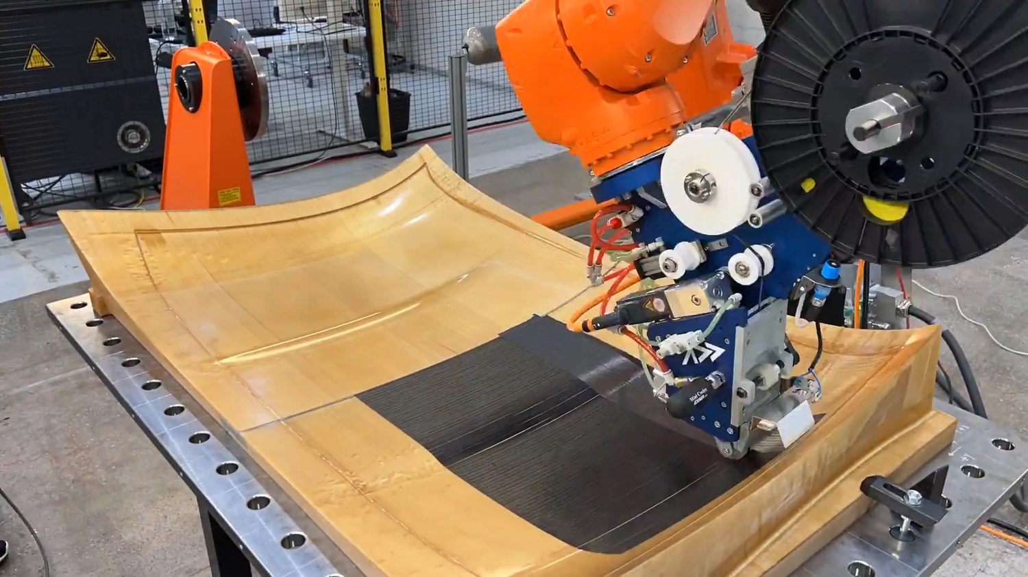 Addcomposites' AFP-XS head depositing tow onto a double-curvature mould, illustrating the surface complexity and conforming layup required for geometrically complex parts such as multi-rib control surfaces.