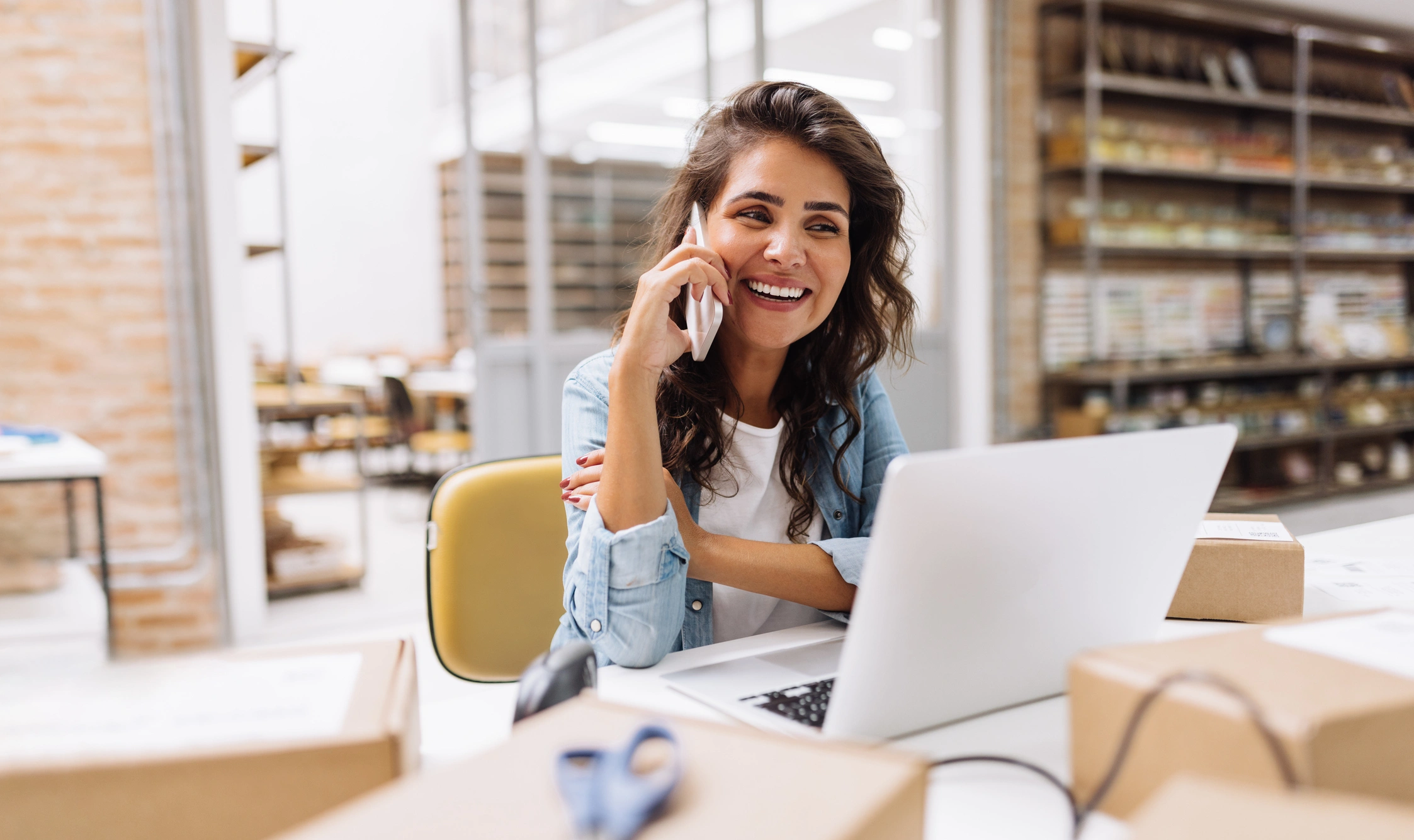 user on the phone with laptop on the table infront of her
