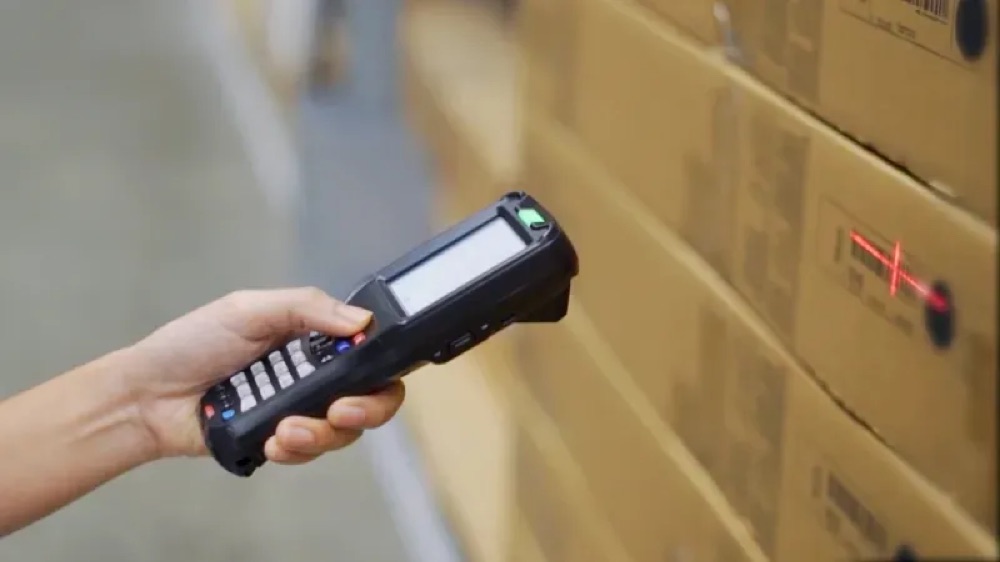 Operative scanning cartons on racking with a ruggedised handheld, representing a combined pick, pack and despatch workflow