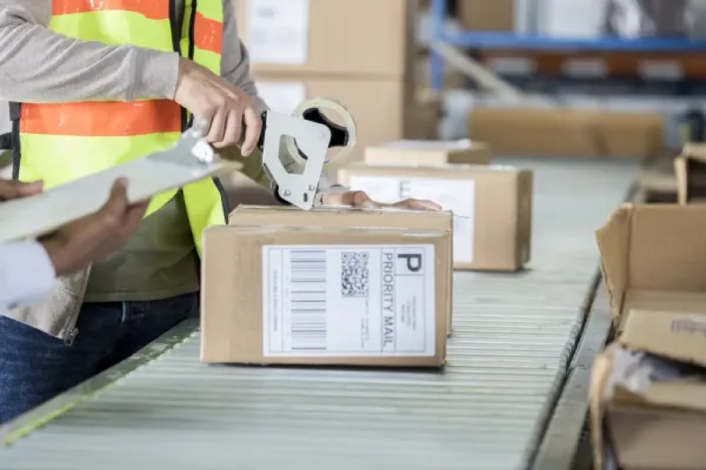 Operative sealing and labelling a parcel on a conveyor, representing a custom repacking workflow