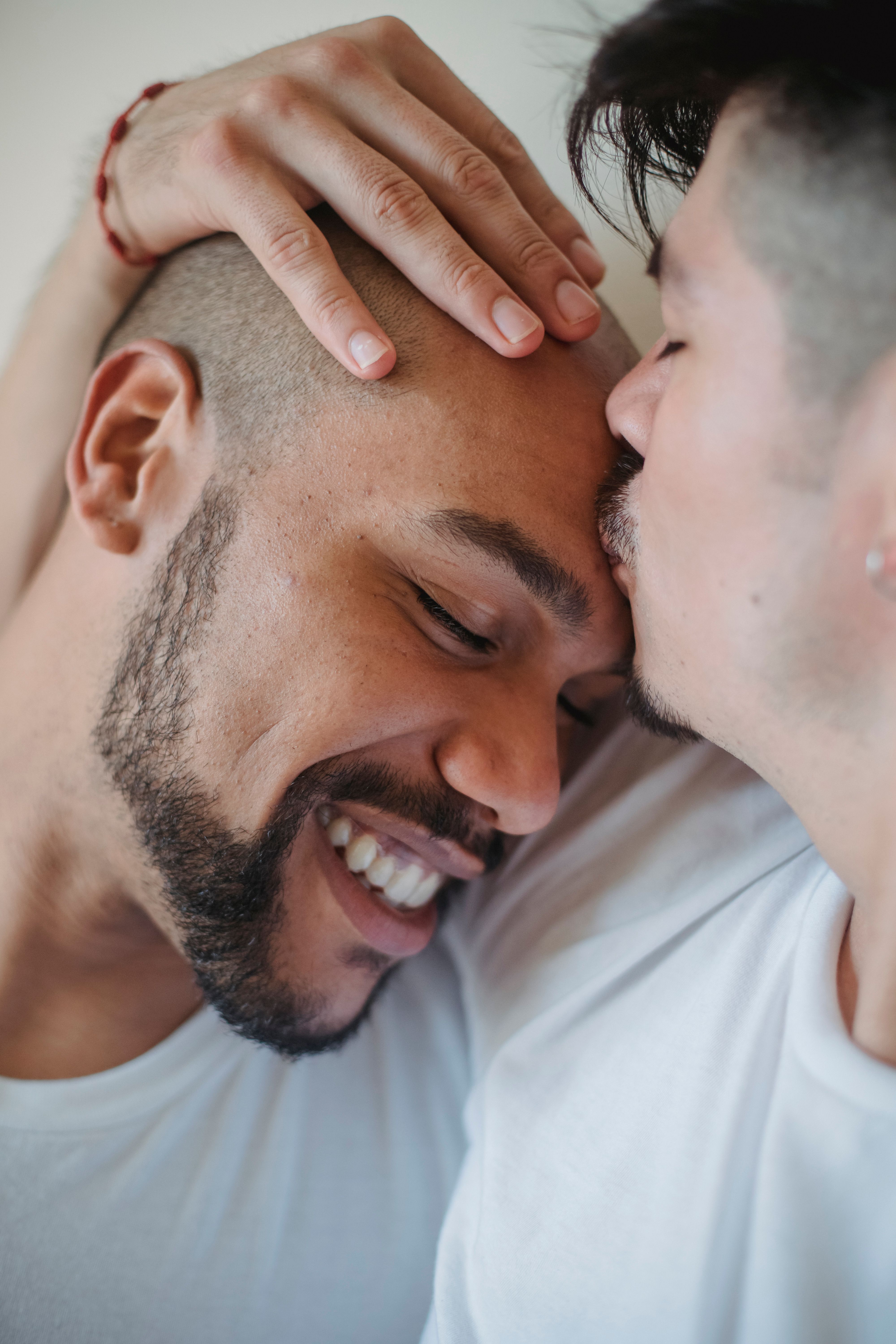 One man kissing another on the forehead while the other laughs warmly.