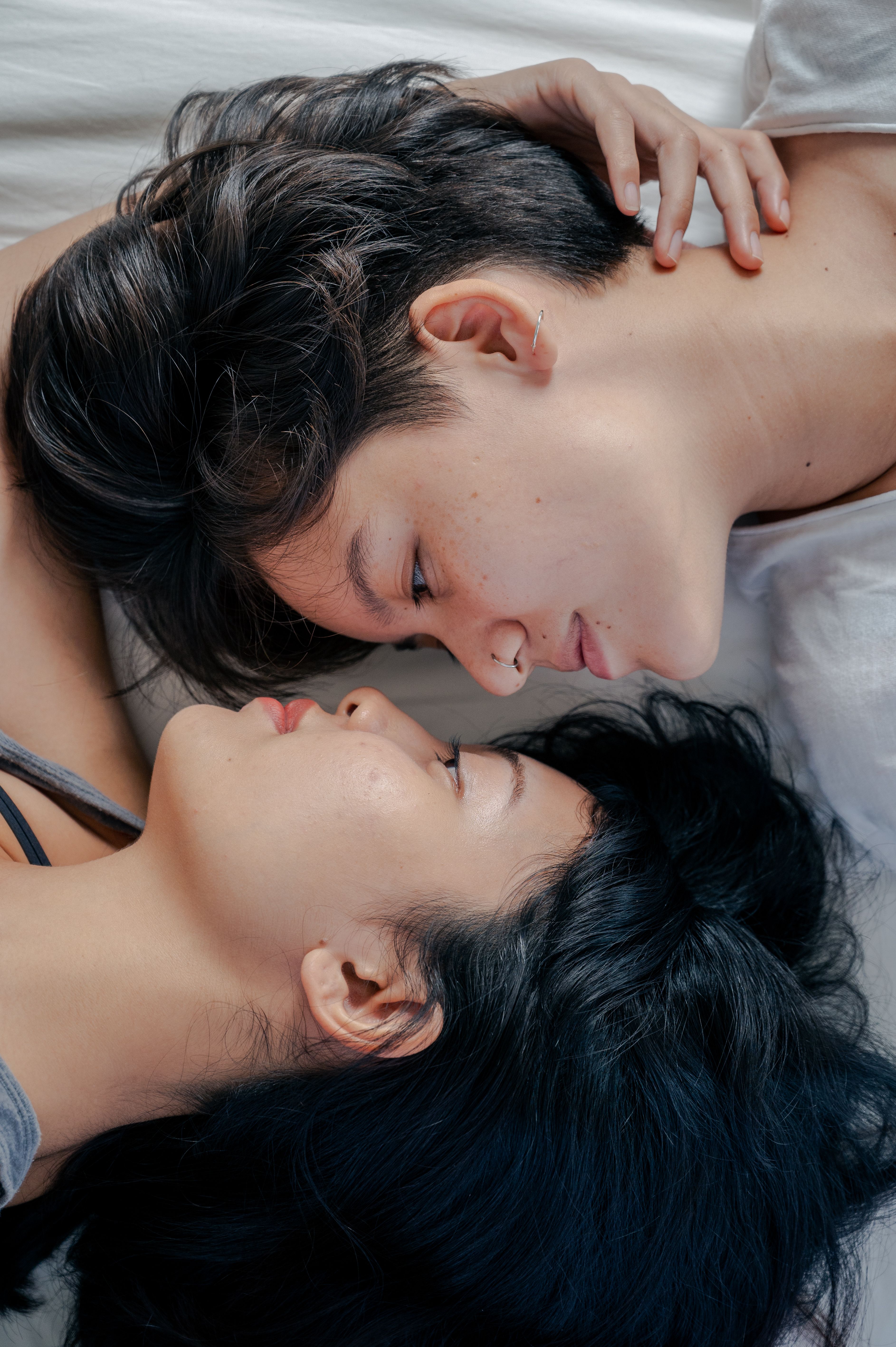 Two people lying on a bed with their faces close together, eyes closed.