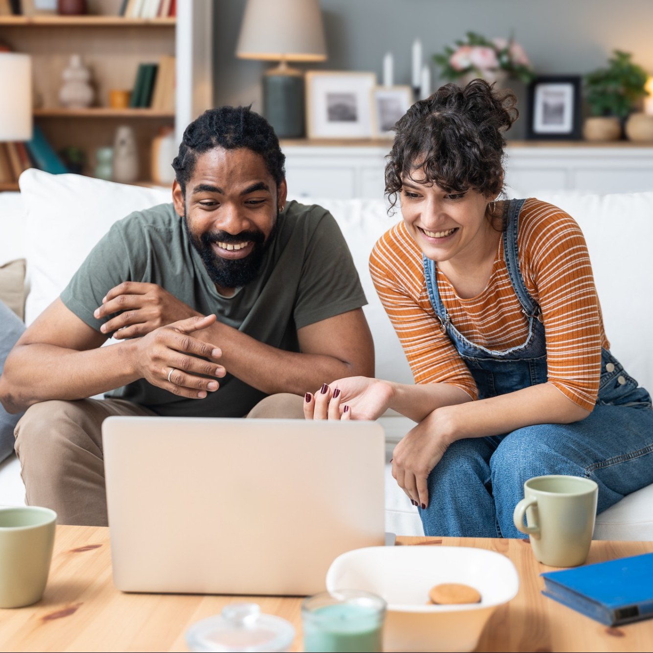 A smiling couple sits together on a couch, looking at a laptop during a virtual session.