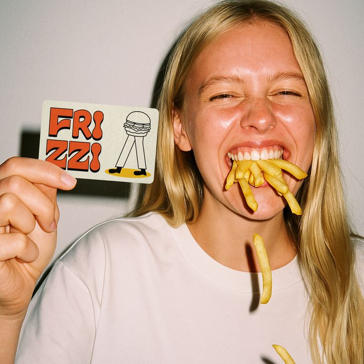 Girl with a mouth full of fries holding a FRIZZI card at Bag Lady's Fry Joint