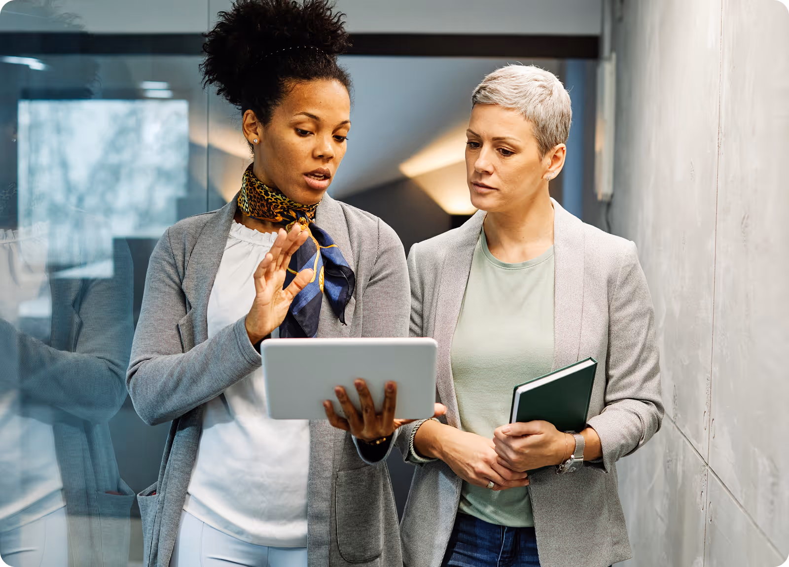 two women walking down a hallway looking at a tablet