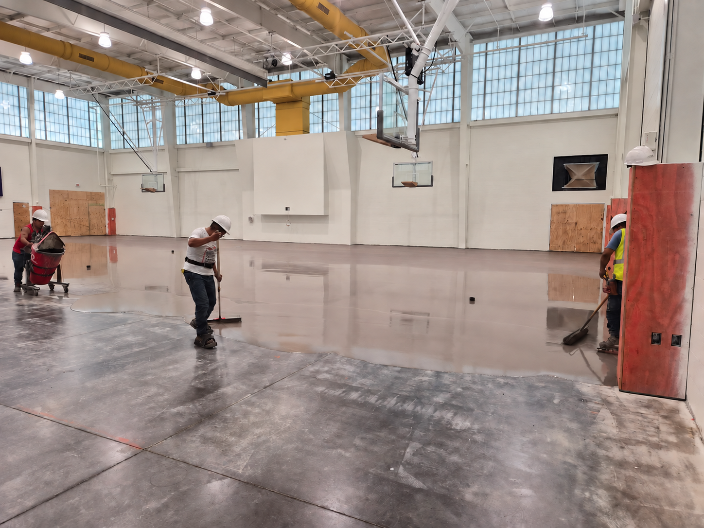 Crew applying self-leveling underlayment across a gymnasium floor