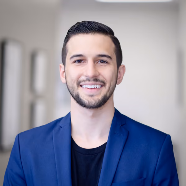 Smiling man with short dark hair and beard wearing a blue blazer and black shirt.